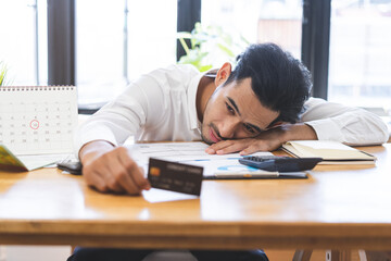 Financial concept, owe asian young male sitting suffer, stressed and confused by calculate expense from invoice, holding mock up credit card, no money to pay mortgage or loan. Debt, bankrupt people.