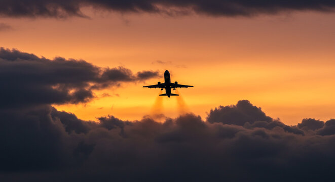 A majestic jet ascends through fiery sunset clouds, a breathtaking silhouette against the vibrant sky.