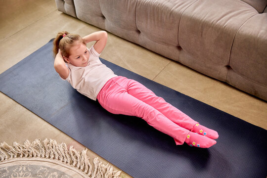 Focused child performing sit-ups on yoga mat during fun physical education class at home. Concept of childhood, online education, remote studying, comprehensive development, sport, health