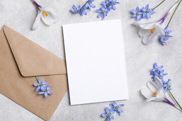 Vertical blank card mockup with kraft envelope, white crocus and blue spring flowers on light...
