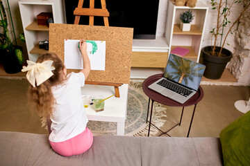 Girl recreating palm tree from laptop screen, using green paint, studying nature through digital...