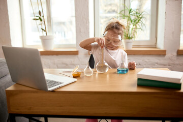 Focused girl, junior school student sitting at wooden desk at home with laptop, having online...