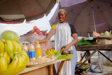 Young African woman selling fruits, wearing white apron and arranging her fruits for buyers