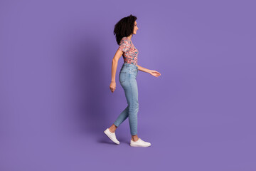 Young woman with curly black hair walks confidently in casual fashion against a purple backdrop, showcasing joy and trendy style