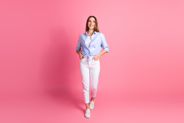 Young happy woman in casual clothing walking confidently against vibrant pink background