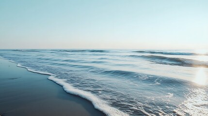 Serene sunrise over calm ocean waves lapping a sandy shore.