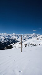 Fototapeta premium Snow-covered Landscape with a Single Vertical Pole Standing Out Against Majestic Mountain Range and Clear Blue Sky