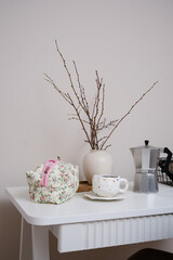 A beautifully serene table display that features delicate branches in ceramic vase, an elegant mug, and a charming bag, copybook, candle.