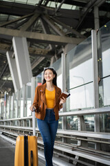 Happy young asian woman traveler using smartphone and holding boarding pass while standing at the airport terminal ready for vacation trip, smiling female tourist with confidently travel insurance