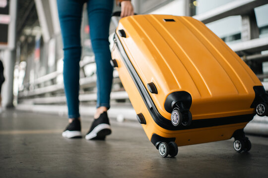 Close up of unrecognized woman tourist walking with her luggage through international airport terminal during holiday trip, female tourist rolling suitcase alone.