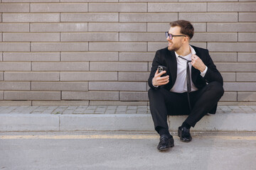 Stressed businessman loosening his tie and using smartphone on the street
