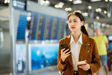 Stressed young asian businesswoman traveler confused missing flight and using smartphone to check flight information and holding passport and boarding pass standing in the airport terminal.