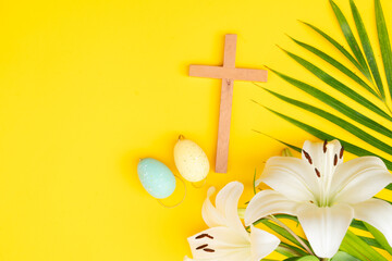 A wooden cross with eggs and lilies on a palm leaves pattern, a Palm Sunday theme.