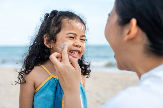 Asian mom applying sunscreen to her happy child’s face on the beach for skin protection from the sun. a young mother carefully smears protective cream on her daughter’s face for safe outdoor fun.