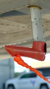 Remove before flight pitot tube cover under the wing of a parked airplane, protection for air speed measuring instrument, red warning flag on aircraft, closeup view