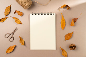 Empty notebook with autumn leaves on beige background. Flat lay, top view.