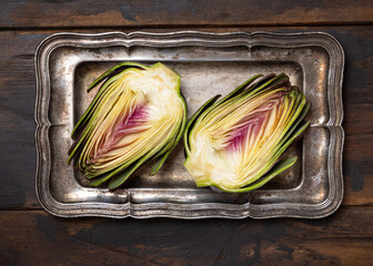 Cut purple raw roman artichokes on a dark wooden table top view. Fresh italian vegetables