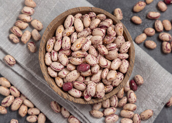 Wooden bowl full of dried pinto beans on napkin on gray top view. Traditional Latin American legumes