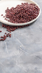 Plate full of dried red azuki beans on gray closeup. East Asian legumes, vegetarian protein source