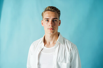 Naklejka premium Confident young man in white shirt posing against light blue background in bright studio setting for fashion or lifestyle concept image.