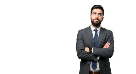 A confident businessman in a suit stands with arms crossed, gazing upward as he contemplates a business issue with a slightly puzzled expression.