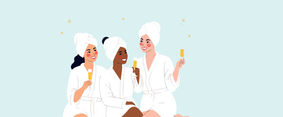 three smiling women in white bathrobes enjoy champagne together