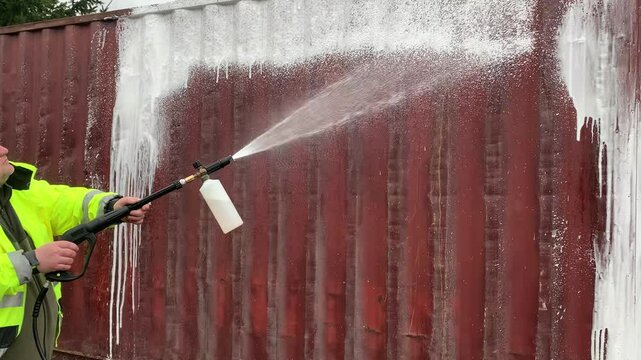 Cleaner in work clothes applies a cleaning agent to the surface of a shipping container.