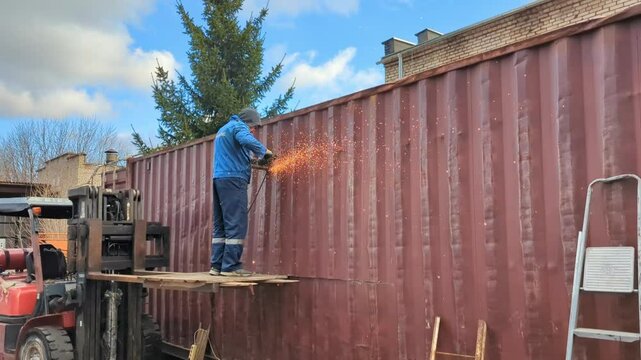 A worker cuts a shipping container with a metal saw.