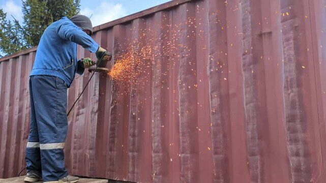 A worker cuts a shipping container with a metal saw.