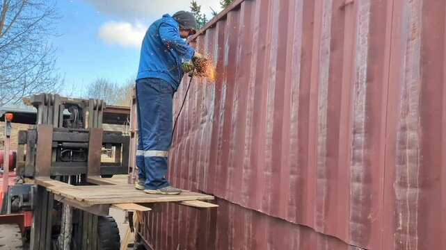 A worker cuts a shipping container with a metal saw.