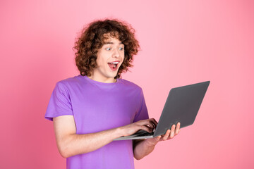 Excited young man in a purple t-shirt enthusiastically using a laptop over a vibrant pink...