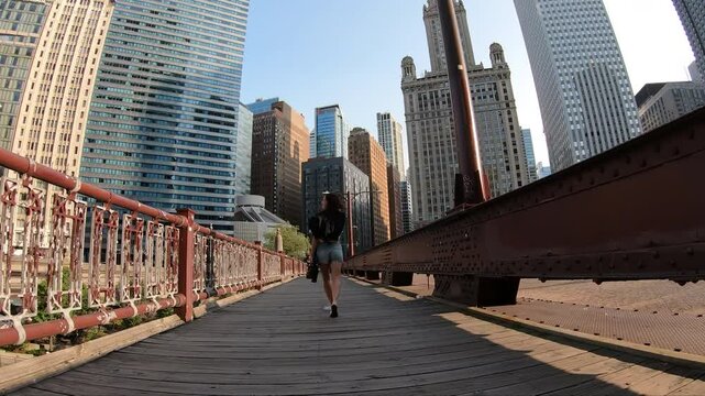 A woman walks confidently across a bridge in Chicago, framed by the towering skyline and warm urban morning light.