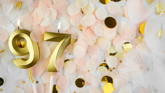97th birthday card. Golden candles number 97, figure ninety-seven on pastel confetti background. Celebrating anniversary and birthday concept.