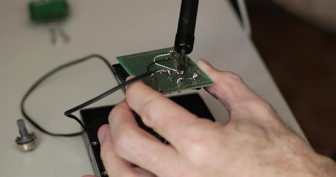 Expert hands performing detailed soldering on PCB. Extreme close-up of microelectronics components and perfect solder joints. High-tech repair process with focus on quality and precision.