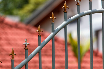 A wrought iron fence with gold spikes and a red roof in the background