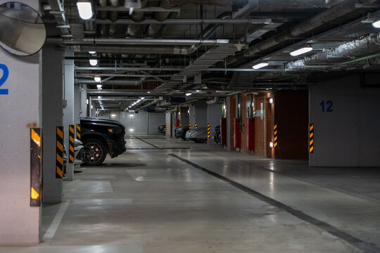 Underground auto park facility with multiple spots and black automobile on left, ceiling is loaded with many pipes and utilities
