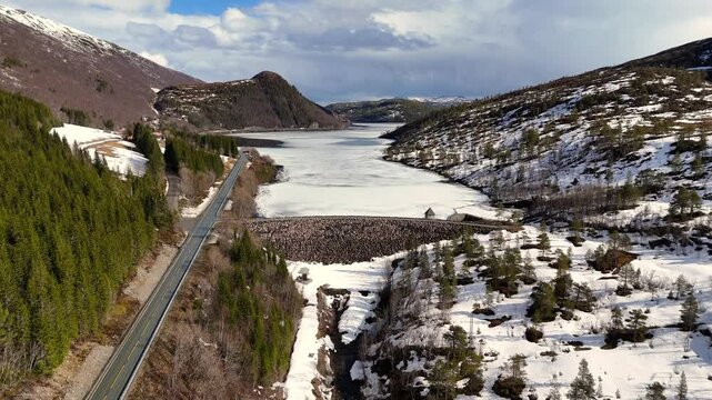 The frozen lake Vasslivatnet and dam with parallel road surrounded by snowy hills and forests