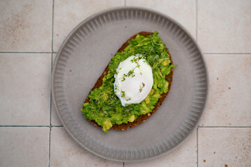 Avocado toast with egg on plate, light tile table