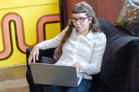 Young woman sit on couch, attentively looking at laptop screen with thoughtful expression, watching educational or informative content, following tutorial, attending webinar, or reading article