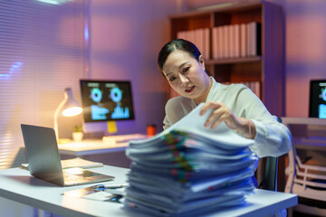 Stressed businesswoman working late at night in office searching through a large pile of paperwork