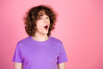 Young curly-haired man in a purple t-shirt showcasing a surprised facial expression against a...