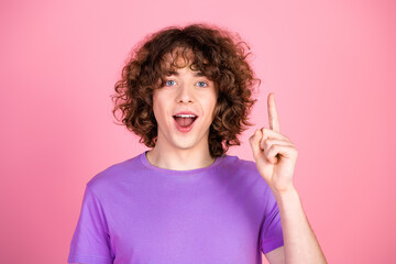 Cheerful young man with curly hair wearing a purple shirt showing positive gesture against a...