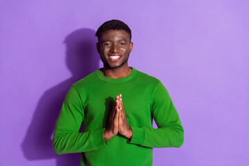 Smiling young man in a green sweatshirt making a hand gesture against a violet background,...