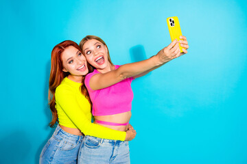 Two joyful girlfriends taking selfie against a turquoise backdrop, capturing cheerful summer vibes...