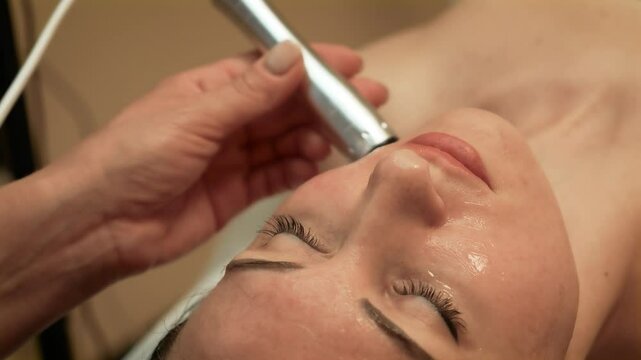 Device performing Ultrasound Fat Reduction on cheek area of client. Specialist applying High-Frequency Facial Therapy for skin toning on upper face. Professional using Microcurrent Lifting Treatment