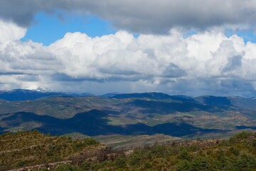 Lush green hills stretch beneath a vast sky filled with dramatic clouds on a clear day in the mountains.
