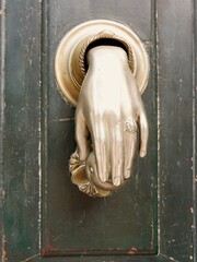 striking hand-shaped door knocker is mounted on a wooden door, featuring intricate details.