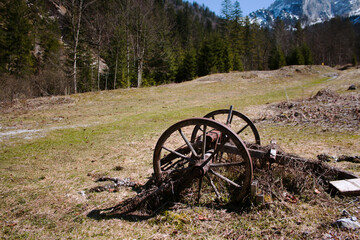Fototapeta premium Old wagon wheel rests in a mountain valley with snowy peaks.