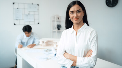 Closeup of female professional architect engineer cross arms with confident while skilled coworker focus on drawing blueprint at table with house model. Creative living and design concept. Immaculate.
