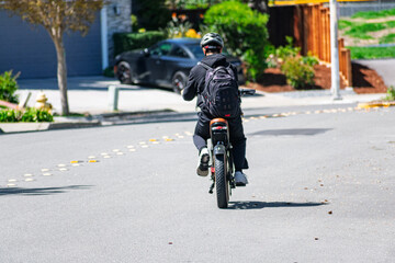 Rear view of a cyclist wearing a helmet and backpack on an e-bike traveling along a residential road